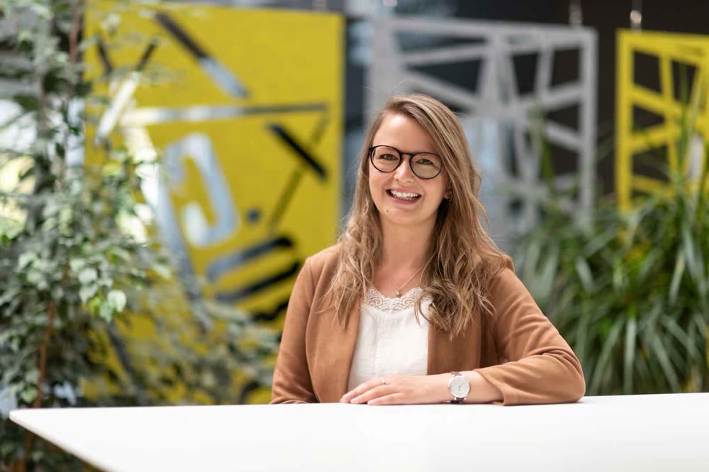 Porträt von Sabrina Stöckli, Payroll-Spezialistin, lächelnd vor einer gelben Wand